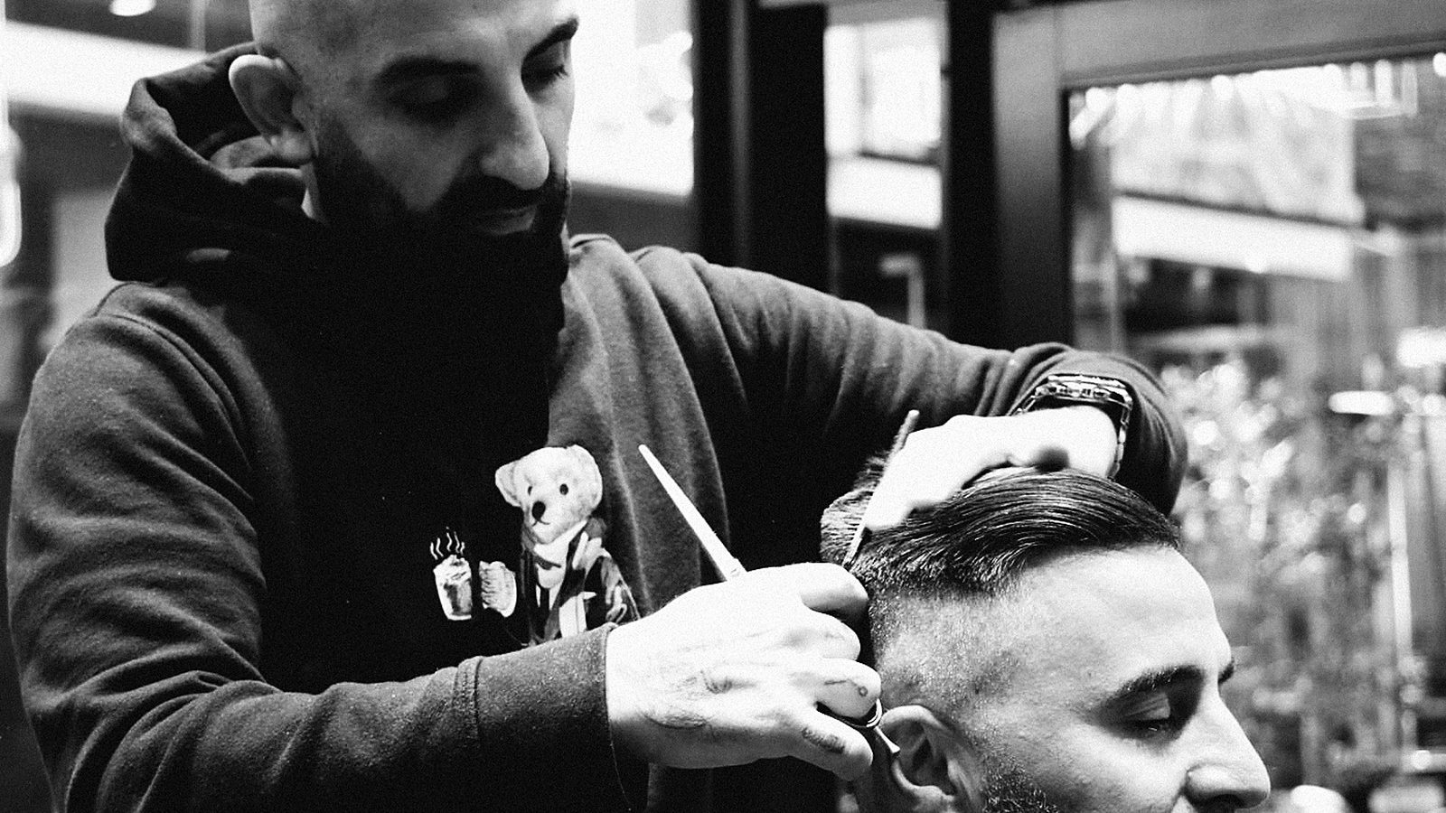 A barber cutting a client's hair with scissors and comb at Sydney Barbers